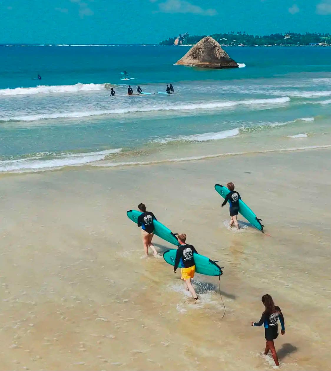 Surfers carrying turquoise boards into the water at Weligama